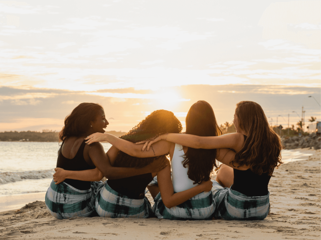 4 tween girls on beach arms around each other facing the setting sun
