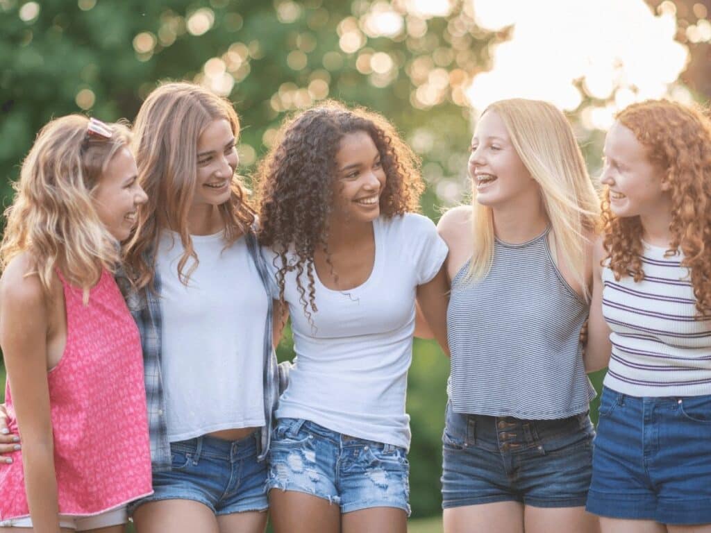 5 girls with arms around each other looking at each other.