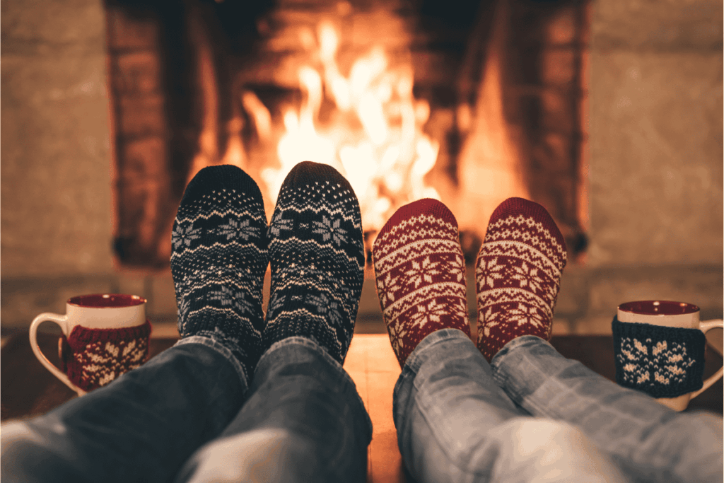 A parent and teen relaxing by a cozy fireplace with holiday socks and warm drinks, representing connection and rest.
