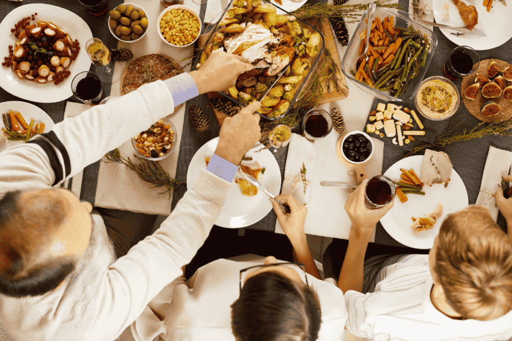 An overhead view of a festive holiday dinner table with family members serving food, highlighting the busy and social nature of holiday gatherings.