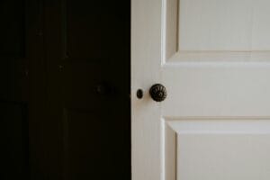 Closed white bedroom door with a dark doorknob, seen from a dim hallway.