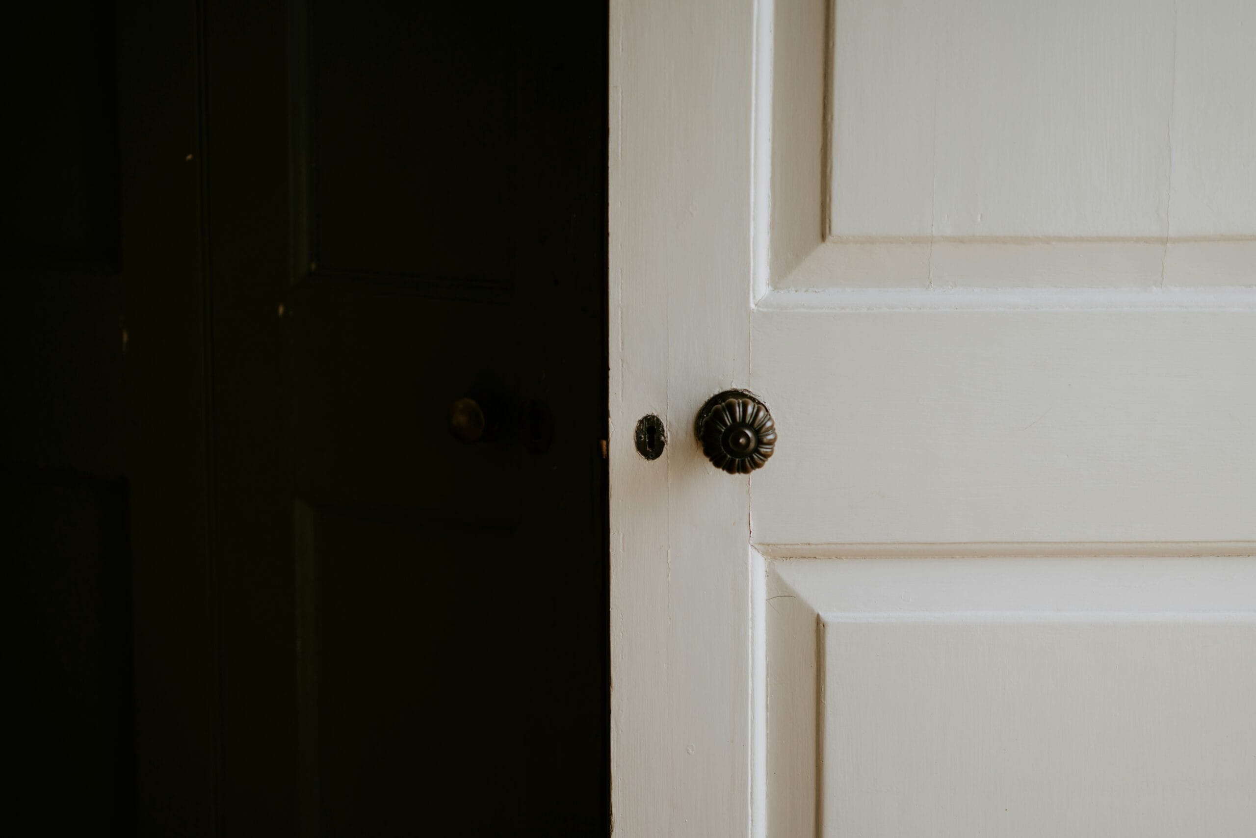 Closed white bedroom door with a dark doorknob, seen from a dim hallway.