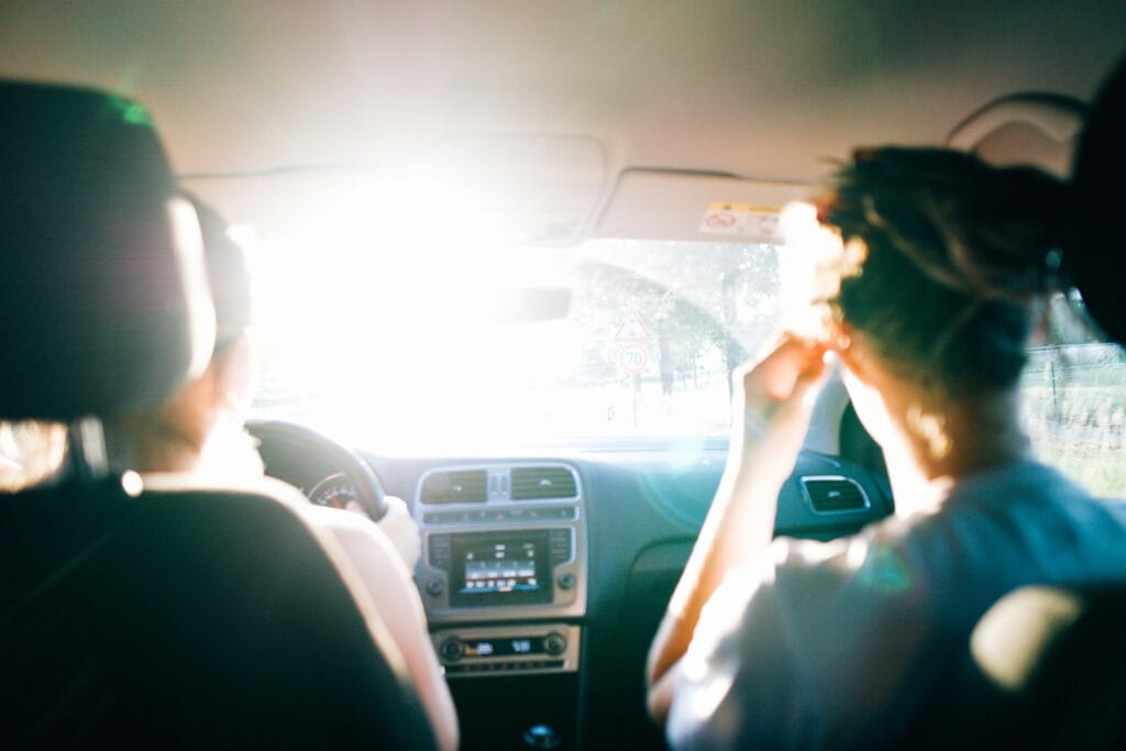 Two people in a car, seen from behind, driving toward bright sunlight.