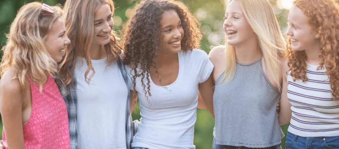 5 girls with arms around each other looking at each other.